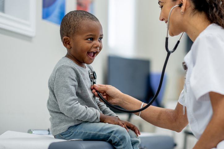 A young boy sits up on an exam table as a female Paediatrician preforms a check-up on him